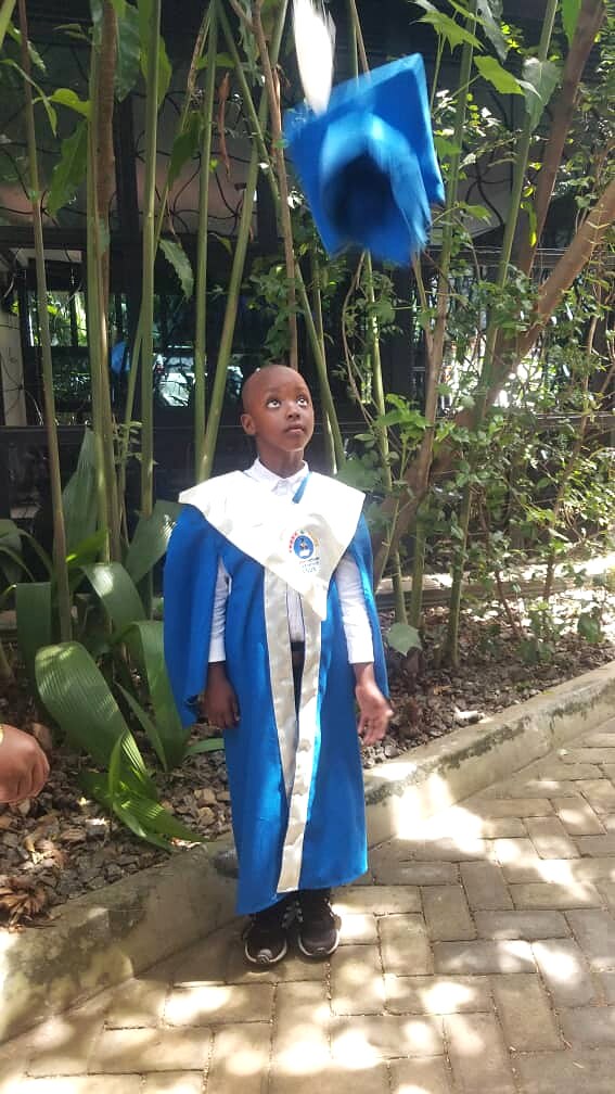 A learner in a blue graduation robe stands outdoors.