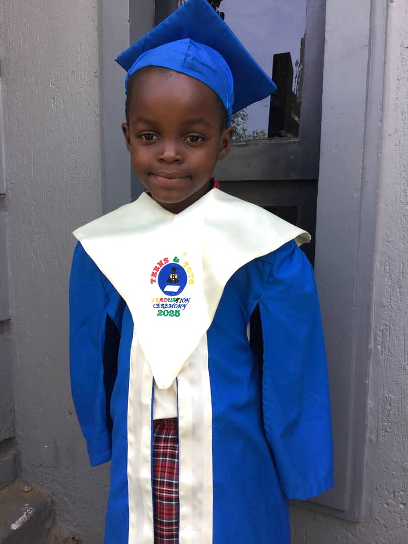 A young learner wears a blue graduation gown and cap.